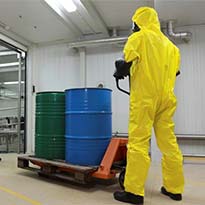 Worker wearing PPE while transporting hazardous chemicals in barrels